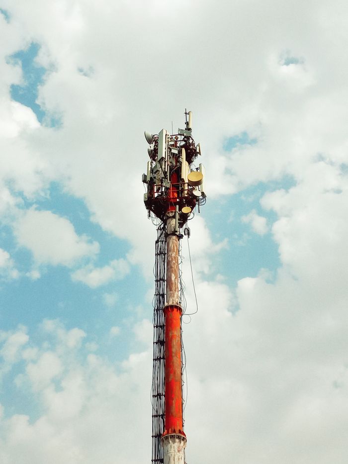 Low-angle view of a cell tower against a cloudy blue sky in Lahore, Pakistan.