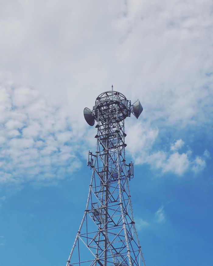 Upward view of a radio tower with a blue sky and clouds, capturing modern telecommunications infrastructure.