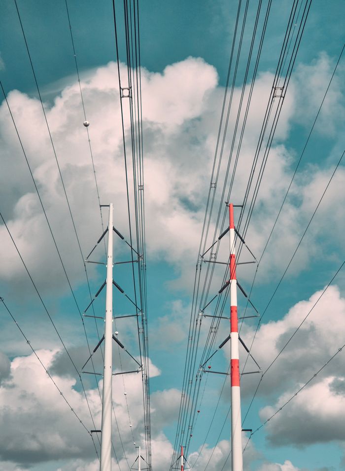 Home Power lines stretch across the sky with fluffy clouds in the background, capturing industrial strength.