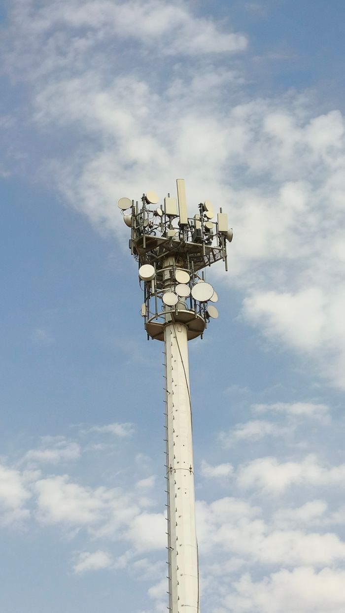 A tall telecommunications tower with antennas under a blue sky with clouds.